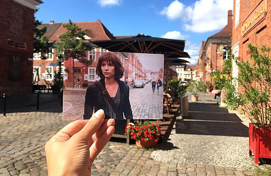 Eine Hand hält ein ausgedrucktes Foto von der Fernsehserie "Homeland" vor einer Einkaufsstraße in Potsdam hoch.