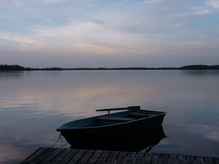 Ein ruhiger See am Abend. Darauf ein leeres Ruderboot, das an einem Steg befestigt ist.