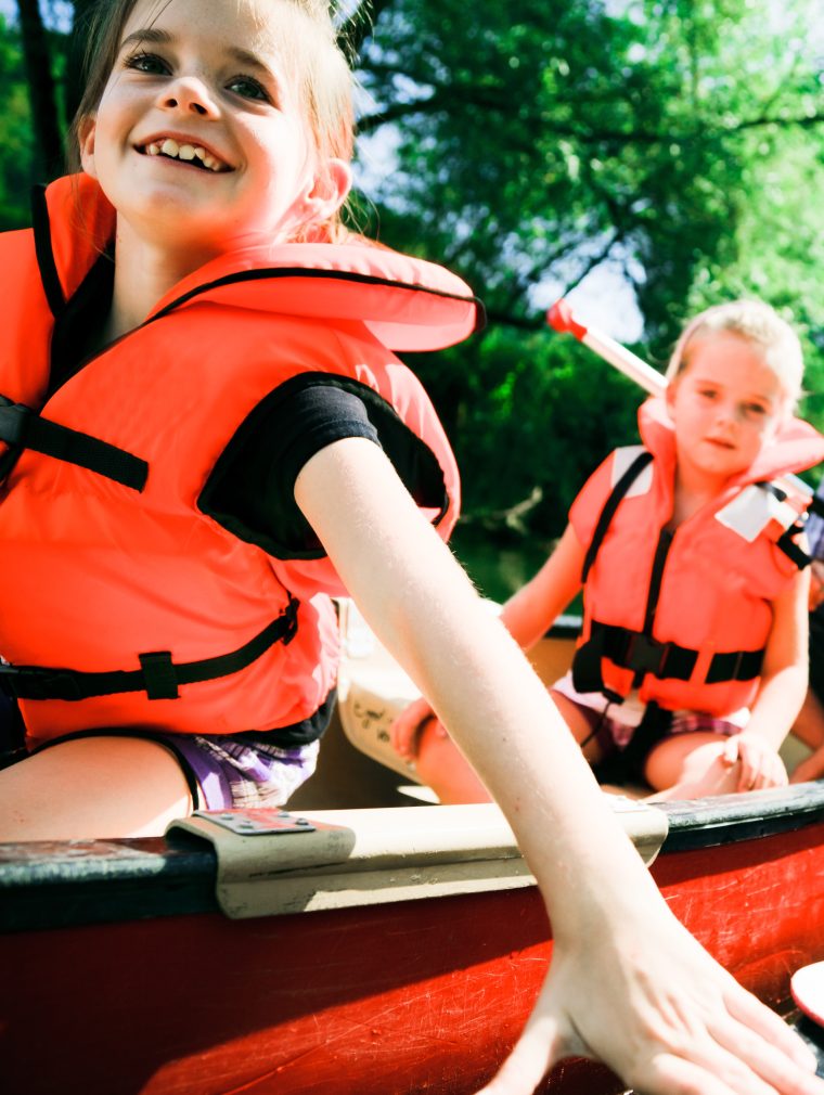 Zwei Kinder und zwei Erwachsene fahren in einem Kanu auf einem Fluss. Sie haben Schwimmwesten an.