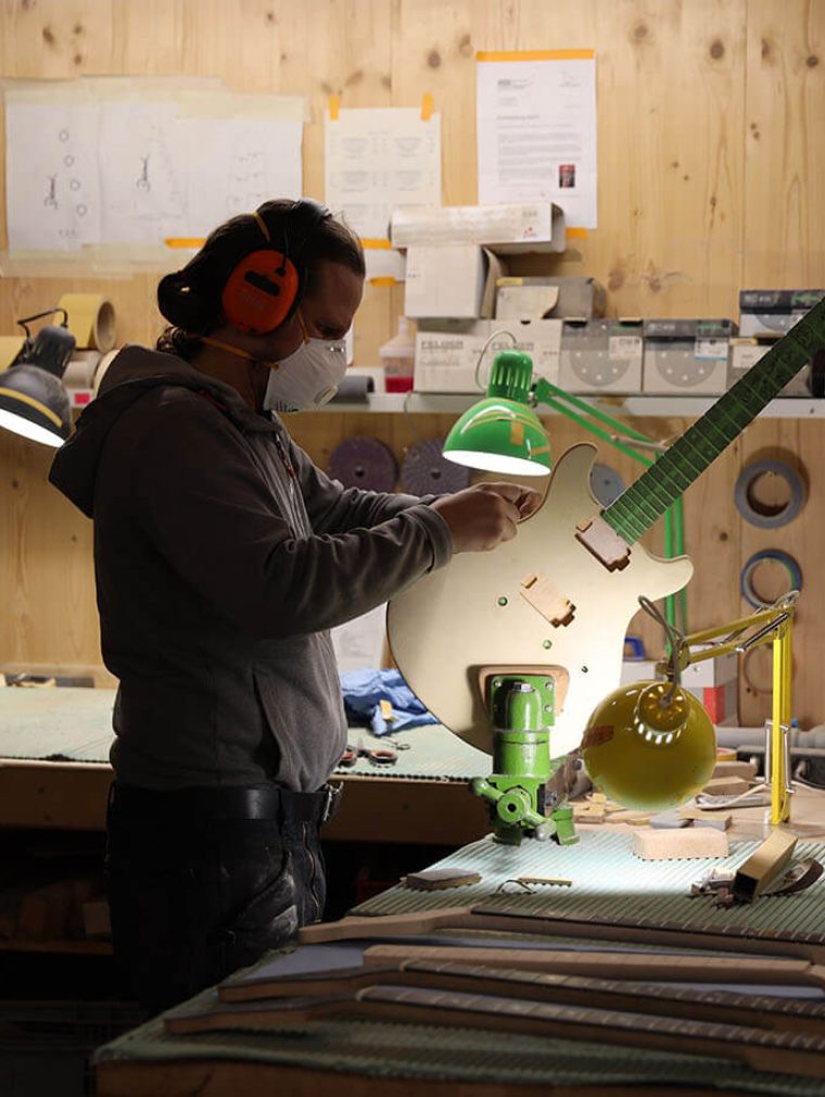 Ein Mann steht in einer Werkstatt und arbeitet an einer E-Gitarre.