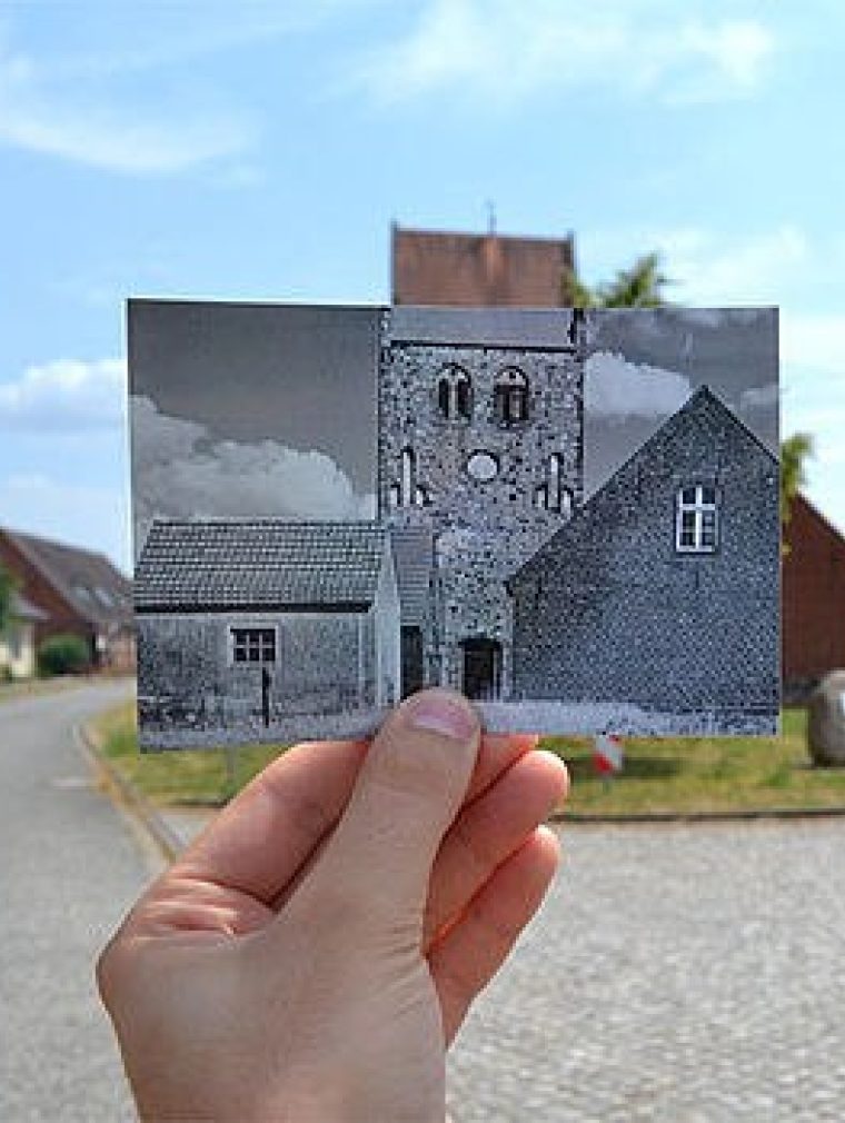 Eine Hand hält ein ausgedrucktes Foto aus dem Film "Das weiße Band" vor einer alten Dorfstraße.