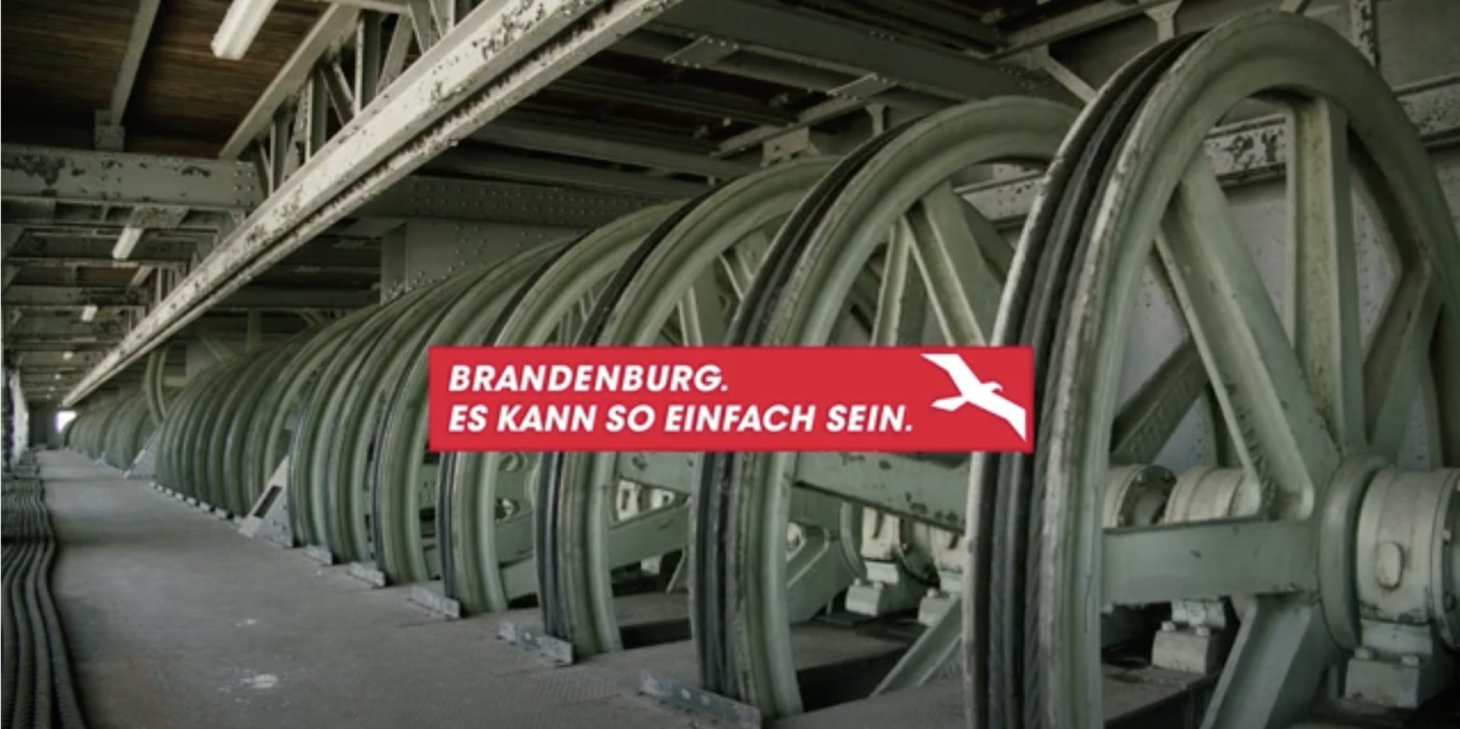 Eine große Fabrikhalle mit Rädern und einer Aufschrift "Brandenburg. Es kann so einfach sein"