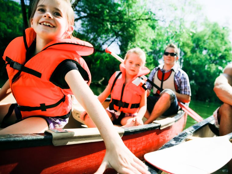 Zwei Kinder und zwei Erwachsene fahren in einem Kanu auf einem Fluss. Sie haben Schwimmwesten an.