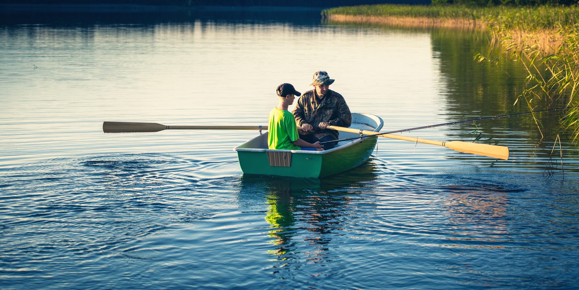 Ein Mann und ein Junge sitzen in einem Ruderboot und paddeln auf einem See.